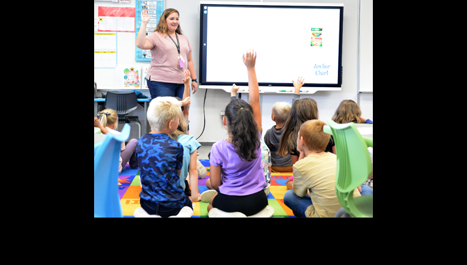 Students raise hands in front of teacher